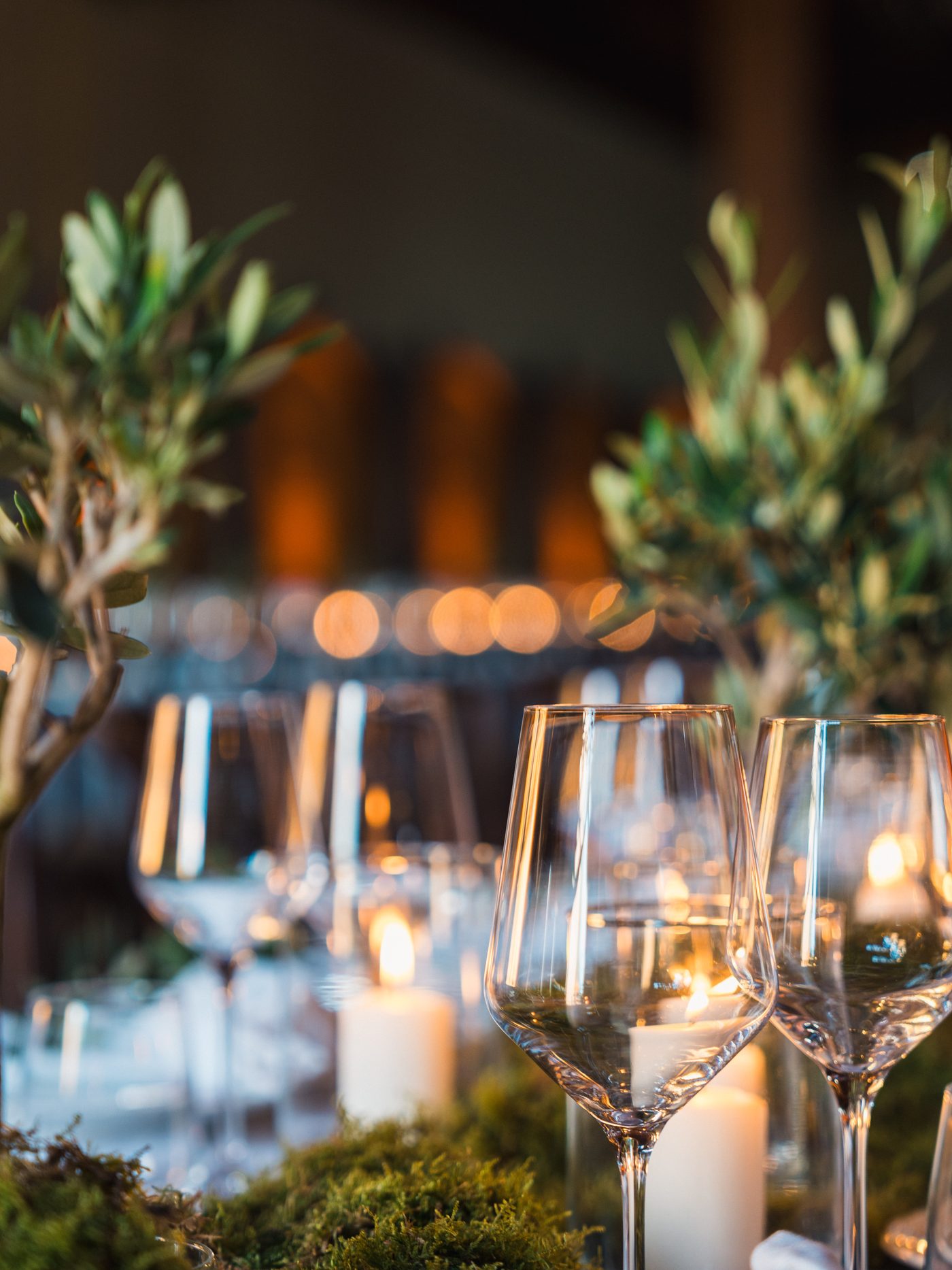 Dettaglio di candele, calici e rametti d'olivo sulla tavola del ricevimento di matrimonio in Toscana